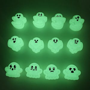 May include: A collection of twelve glowing ghost-shaped decorations with various facial expressions. The ghosts are a pale green color and have black eyes and mouths. The background is a dark green.
