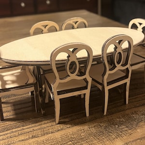 Puede incluir: Un juego de comedor de madera en miniatura con una mesa ovalada y seis sillas. Las sillas tienen respaldos ornamentados y el juego está hecho de madera clara con ribetes oscuros. La mesa mide aproximadamente 30 cm de largo.