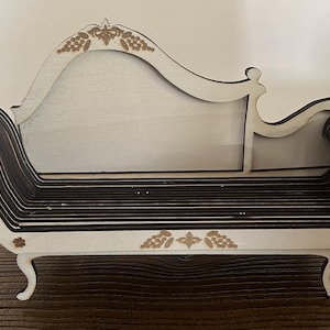 May include: A decorative wooden chaise lounge. The miniature furniture piece is white with dark brown layered seating. The back and arms have a curved design. The piece has decorative floral accents and is supported by curved legs.