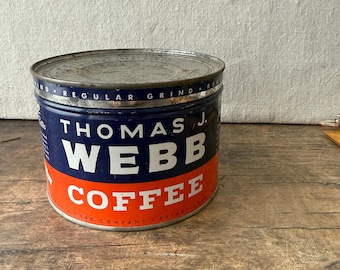 May include: Vintage Thomas J. Webb Coffee tin. The cylindrical tin has a blue and orange color scheme with white lettering. The top of the tin is silver. The text on the tin reads "Thomas J. Webb Coffee".