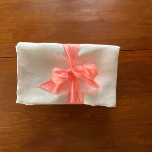 May include: A white linen fabric wrapped in a coral satin ribbon with a bow.