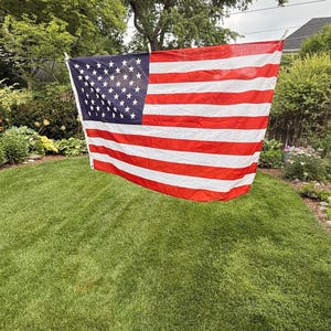 May include: A rectangular United States flag featuring a dark blue canton with white stars in the upper left corner, alongside thirteen alternating horizontal red and white stripes. The flag is suspended horizontally by clips on a clothesline.