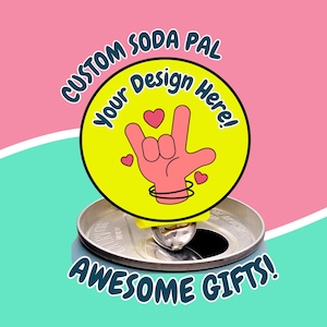 May include: Yellow round sticker with the text "Custom Soda Pal Your Design Here!" and a pink hand making the "I love you" sign with hearts around it. The sticker is on top of a silver can.
