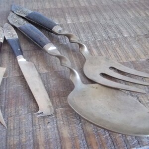 May include: A set of three silver-toned serving utensils with ornate handles. The set includes a spoon, a fork, and a knife. The handles are made of dark wood and have intricate carvings.