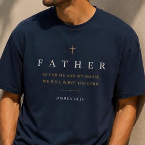 Op de afbeelding: Marineblauwe t-shirt met het woord "FATHER" in witte hoofdletters, een gouden kruis erboven en de quote "AS FOR ME AND MY HOUSE, WE WILL SERVE THE LORD." uit Jozua 24:15. De t-shirt heeft een ronde hals.