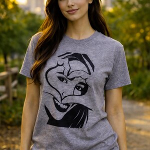 Puede incluir: Una camiseta gris jaspeado de manga corta con un estampado gráfico negro en la parte delantera. El diseño muestra una ilustración estilizada de un rostro con las manos formando un corazón alrededor de los ojos y la nariz, en líneas negras.