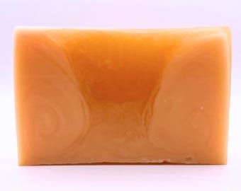May include: A rectangular bar of handmade soap with a translucent, amber-orange color. Swirls of lighter orange and white create a marbled effect throughout the soap. The soap has a smooth, glossy surface.