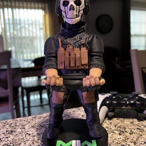 Peut inclure: Figurine d'un personnage du jeu vidéo Call of Duty: Modern Warfare II. La figurine porte une tenue noire, un masque de crâne et un casque. La base de la figurine porte le texte "MWII" en vert et blanc.