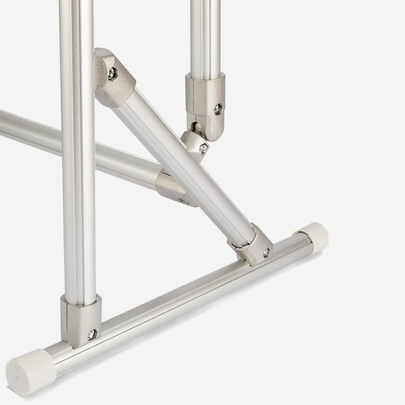 May include: A silver-colored metal frame structure composed of cylindrical tubes connected by metallic joints. The base features white plastic end caps on the horizontal bars, providing stability to the modular assembly of the support system.
