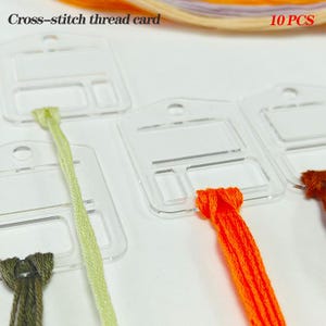 Puede incluir: Tarjetas transparentes de hilo de punto de cruz acrílico con hilo de bordar colorido. Las tarjetas tienen un diseño rectangular con un agujero para colgar y una ranura para sujetar el hilo. El texto "Cross-stitch thread card" y "10 PCS" son visibles.