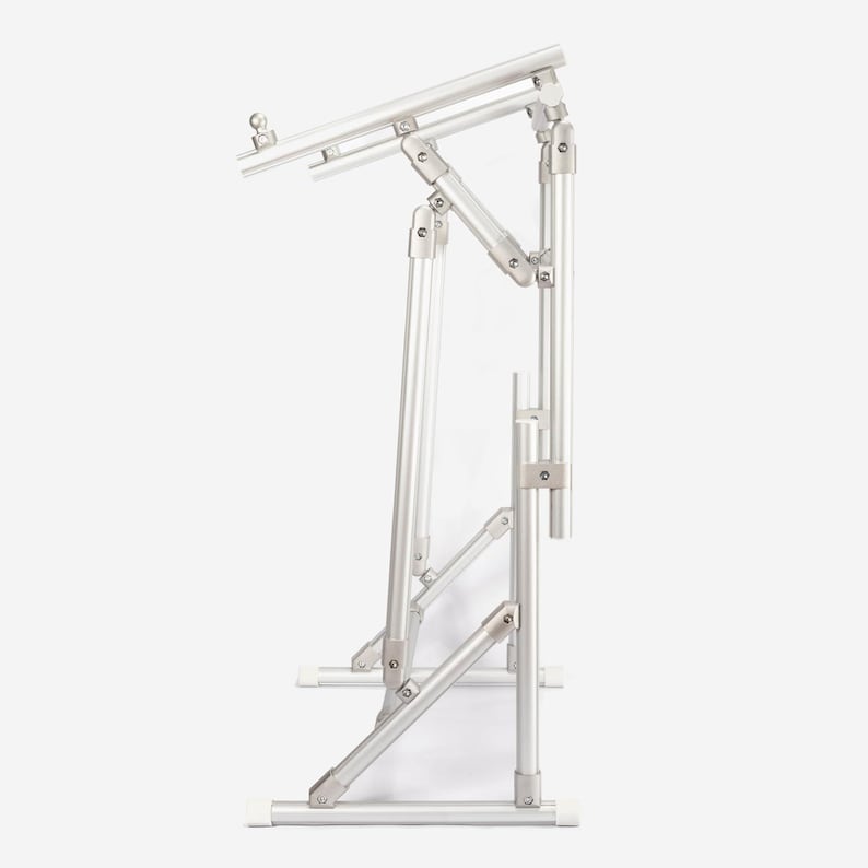 May include: A silver-colored adjustable laptop stand constructed from lightweight metal tubing. The frame features multiple hinged joints and support bars, allowing for height and angle modifications. It has a flat base and a top platform.