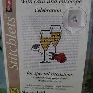 May include: A counted cross stitch kit with a card and envelope. The design features two champagne glasses with a red rose. The kit includes Aida fabric, embroidery threads, a needle, and full charted instructions. The kit is for special occasions and is shown actual size. Stitchlets Celebration Mouseloft © 2005 014-543std