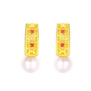 May include: A pair of gold-colored earrings with a filigree design and small red accents. Each earring features a white, round pearl at the bottom, creating a classic and elegant look. The earrings are set against a white background.