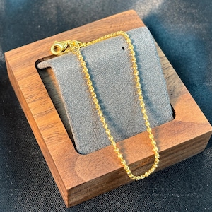 Puede incluir: Una pulsera de cadena dorada que presenta una serie de pequeños eslabones redondos y texturizados que crean una apariencia de cuentas. La pulsera incluye un cierre de langosta en un extremo y un acabado metálico pulido que refleja la luz.