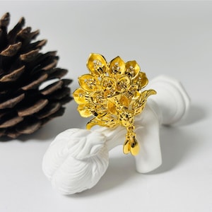 May include: A gold-colored peacock-shaped hair ornament with intricate details. The ornament has a long, dangling tail with a decorative bead at the end.