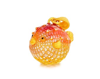 May include: A gold-colored pendant in the shape of a pufferfish. The fish has a red and orange body with a textured, scale-like pattern. The fins and details are gold, and the eyes are black. The pendant has a loop for a chain.