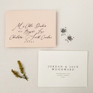 May include: Two white envelopes with black calligraphy. The top envelope is pink and has the address "Mrs. Chloe Dunham, 468 Bayside Lane, Charleston, South Carolina 29401". The bottom envelope has the address "JORDAN & JACK WOODWARD, 468 Springdale Lane, Atlanta, Georgia 30606".