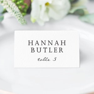 May include: White place card with black text that reads "HANNAH BUTLER table 3".