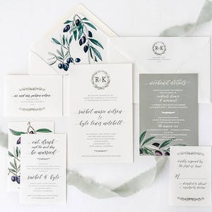 May include: A wedding invitation suite with olive branch illustrations. The invitation features the couple's names, "Rachel Marie Wilson" and "Kyle Lewis Mitchell", and the date of the wedding. The RSVP card includes a checkbox to indicate whether the guest will attend or decline.