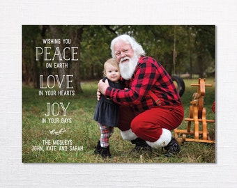 Puede incluir: Una tarjeta de Navidad con un Papá Noel con una camisa a cuadros rojos y negros y pantalones rojos, sosteniendo a una niña pequeña con un vestido a cuadros negros y blancos. La tarjeta tiene el texto "Wishing you Peace on Earth Love in your hearts Joy in your days The Mosleys John, Kate and Sarah".