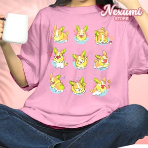 Puede incluir: Camiseta rosa con un patrón repetido de criaturas de dibujos animados parecidas a corgis en varias poses. Los corgis son amarillos, blancos y naranjas con orejas verdes. La camiseta tiene el texto "Nexumi STORE" en la esquina superior derecha.