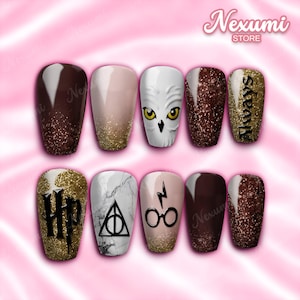 Puede incluir: Un juego de diez uñas postizas con varios diseños, incluyendo una cara de búho blanco, purpurina dorada, degradados marrones, patrón de mármol y símbolos negros. Las uñas muestran el texto HP, Always, un rayo y unas gafas.