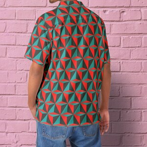Puede incluir: Una camisa de manga corta con botones y un patrón geométrico en tonos rojos, verdes y negros. La camisa tiene cuello y cierre de botones.