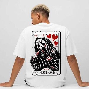 May include: White t-shirt featuring a graphic of Ghostface from the Scream movies. The design includes a black and white illustration of Ghostface holding a bloody knife and a phone, with red hearts and the word "GHOSTFACE".