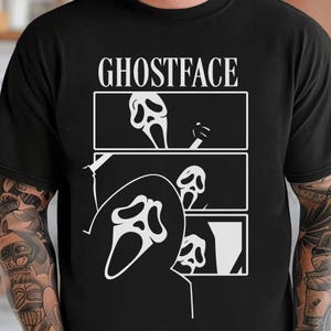May include: Black t-shirt featuring a white graphic of the Ghostface mask from the Scream horror film series. The design includes the word "GHOSTFACE" above three panels with the mask in different poses.