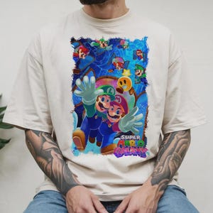 Puede incluir: Camiseta color crema con un gr&aacute;fico vibrante del videojuego Super Mario Galaxy. El dise&ntilde;o muestra a Mario y Luigi con un fondo c&oacute;smico y el logotipo del juego. La camiseta tiene un ajuste c&oacute;modo y holgado.