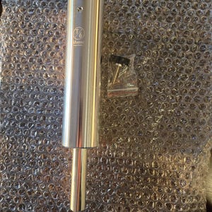 May include: A cylindrical, silver-colored metal object with a smaller, cylindrical extension. The object has the text "T6 Marine" printed on it. A small bag of screws and a black knob are also present.