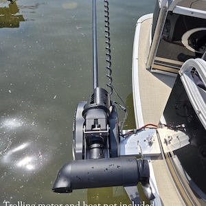 May include: A black trolling motor attached to a boat. The motor is submerged in water and has a long, curved shaft with a propeller. The boat has a beige deck and a black and silver railing. Text on the image: Trolling motor and boat not included.