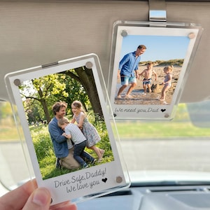 Könnte beinhalten: Zwei transparente Acryl-Foto-Autosonnenblenden-Clips, die jeweils ein Familienfoto zeigen. Ein Clip zeigt einen Vater mit zwei Kindern am Strand, der andere zeigt einen Vater, der zwei Kinder umarmt. Auf den Clips steht "Drive Safe, Daddy! We love you" und "We need you, Dad".