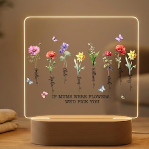 Könnte beinhalten: Ein beleuchtetes Acrylschild mit Holzsockel zeigt farbenfrohe Blumenillustrationen und den Text "If mums were flowers, we'd pick you." Schmetterlinge und Namen sind ebenfalls enthalten.