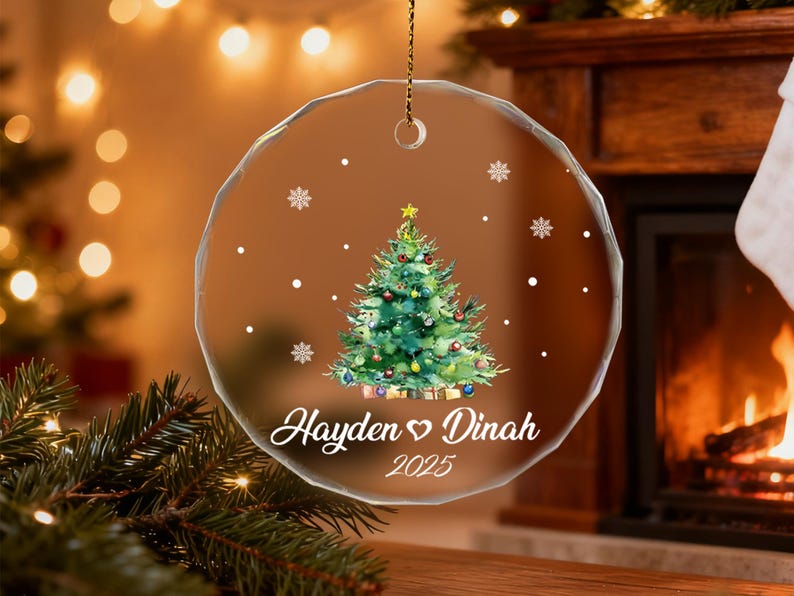 Pu&ograve; includere: Ornamento natalizio rotondo e trasparente con un design ad acquerello di un albero di Natale, fiocchi di neve e i nomi "Hayden ♡ Dinah" e l'anno 2025. L'ornamento &egrave; appeso a una catena d'oro.