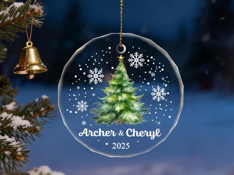 Pu&ograve; includere: Un ornamento natalizio rotondo e trasparente con un design ad acquerello di un albero di Natale, fiocchi di neve e i nomi "Archer & Cheryl" con l'anno "2025". L'ornamento &egrave; appeso a una catena d'oro.