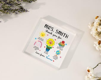 May include: A white acrylic block with a colorful illustration of a sunflower and other school-related icons. The text "MRS. SMITH thank you for..." is at the top of the block. The text "Love from Thomas" is at the bottom of the block.