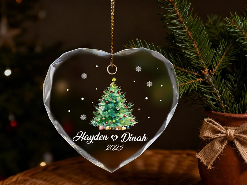Pu&ograve; includere: Ornamento natalizio a forma di cuore con un design festivo a forma di albero di Natale. L'ornamento in vetro trasparente presenta un albero di Natale verde con ornamenti colorati e i nomi "Hayden & Dinah" e l'anno "2025". Una catena d'oro &egrave; attaccata per appenderlo.