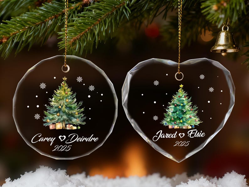 Pu&ograve; includere: Due decorazioni natalizie in vetro trasparente, una rotonda e una a forma di cuore, ciascuna con un disegno di albero di Natale dipinto. L'ornamento rotondo riporta i nomi "Carey & Deirdre 2025" e l'ornamento a forma di cuore riporta i nomi "Jared & Elsie 2025".