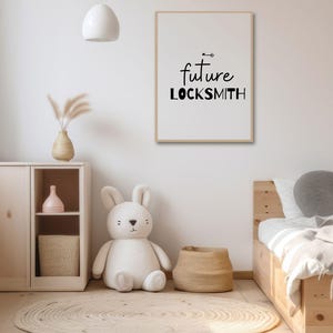 Puede incluir: Una impresión enmarcada en blanco con texto negro que dice "future locksmith" con una pequeña flecha sobre la palabra "future". La impresión está colgada en una pared blanca en una guardería con un conejito de peluche blanco, un estante de madera y una cama de madera.