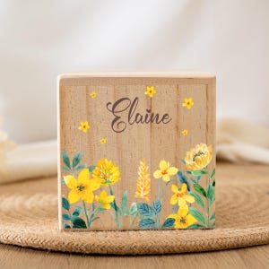 May include: A wooden box with a floral design featuring yellow flowers and green leaves. The box is personalized with the name "Elaine" in brown lettering.