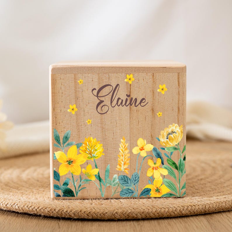 May include: A wooden box with a floral design featuring yellow flowers and green leaves. The box is personalized with the name "Elaine" in brown lettering.