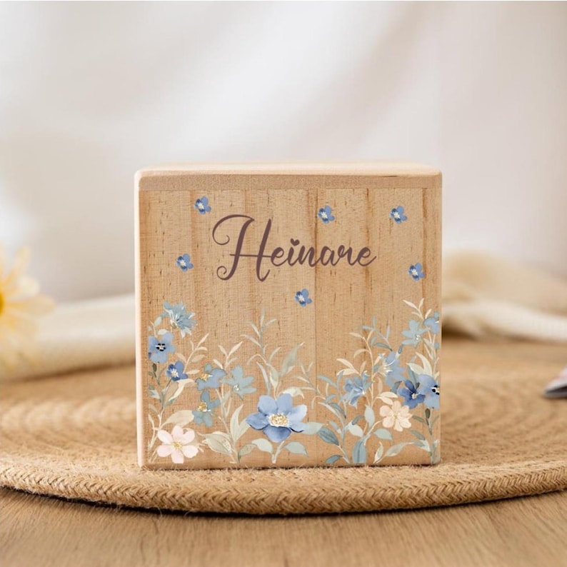 May include: A wooden box with a floral design and the name "Hein&auml;me" written on it. The flowers are blue, white, and green.