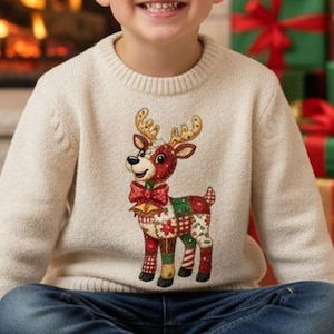 Könnte beinhalten: Ein Kind trägt einen cremefarbenen Weihnachts-Pullover mit einem Rentier-Design, einer roten Fliege und Patchwork-Mustern. Das Kind sitzt auf einem weißen Teppich vor einem Kamin und verpackten Geschenken.