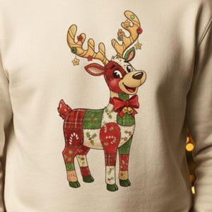 Könnte beinhalten: Cremefarbenes Sweatshirt mit einem Cartoon-Rentier-Design. Das Rentier hat eine rote Nase, eine rote Fliege und einen Körper im Patchwork-Stil in Rot, Grün und Weiß. Die Geweihe sind mit goldenen Akzenten und Sternen verziert. Ein festliches Kleidungsstück zum Thema Feiertage.