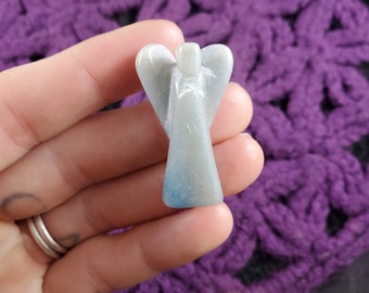 May include: A small, carved angel figurine made of light blue and white stone. The angel has a simple design with outstretched wings and a long, flowing robe.