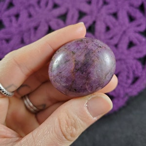 May include: A smooth, polished purple and black gemstone sphere. The sphere has a natural, organic look with a variety of textures and patterns.