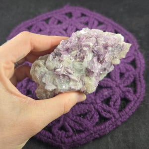 May include: A cluster of purple and white lepidolite crystals. The crystals are clustered together in a rough, natural formation.