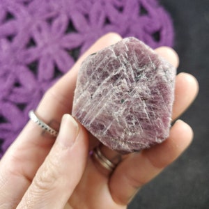 Peut inclure: Un cristal de rubis rose avec une surface brute et facetée. Le cristal est d'une couleur rose foncé avec une légère teinte violette. Il a un aspect naturel et non poli.