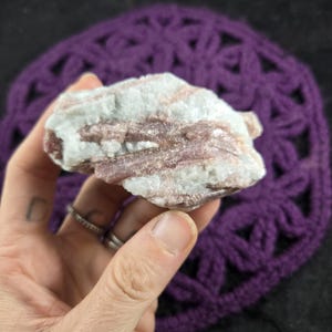 May include: A raw mineral specimen featuring elongated, dusty rose-colored crystals embedded within a matrix of opaque, milky white quartz. The stone has a rough, uneven texture with visible striations along the length of the pink crystal formations.